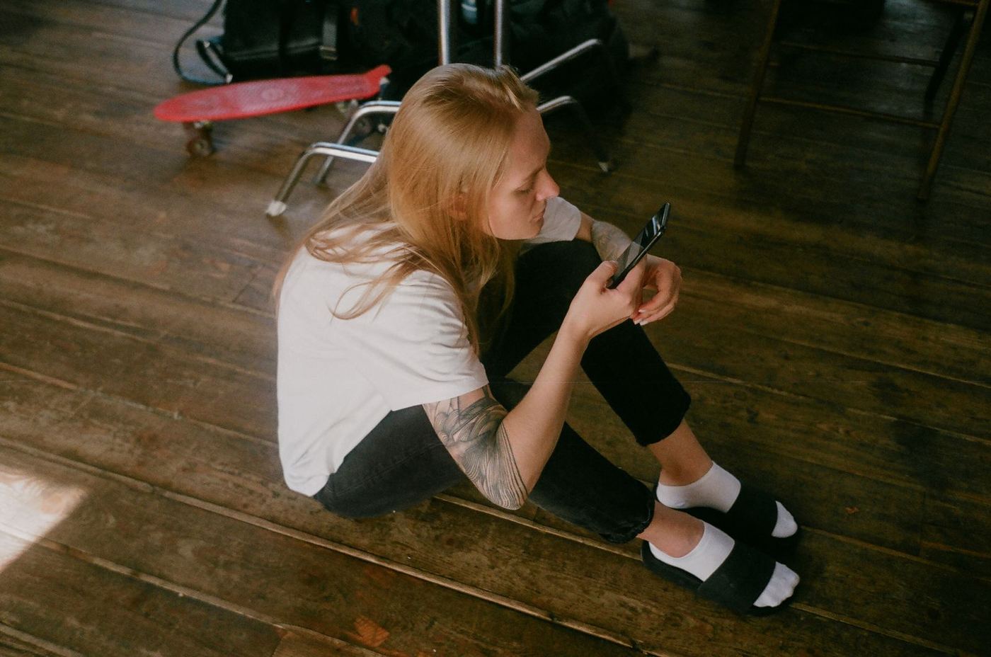 Une artiste tatouée, assise par terre, consulte son téléphone.