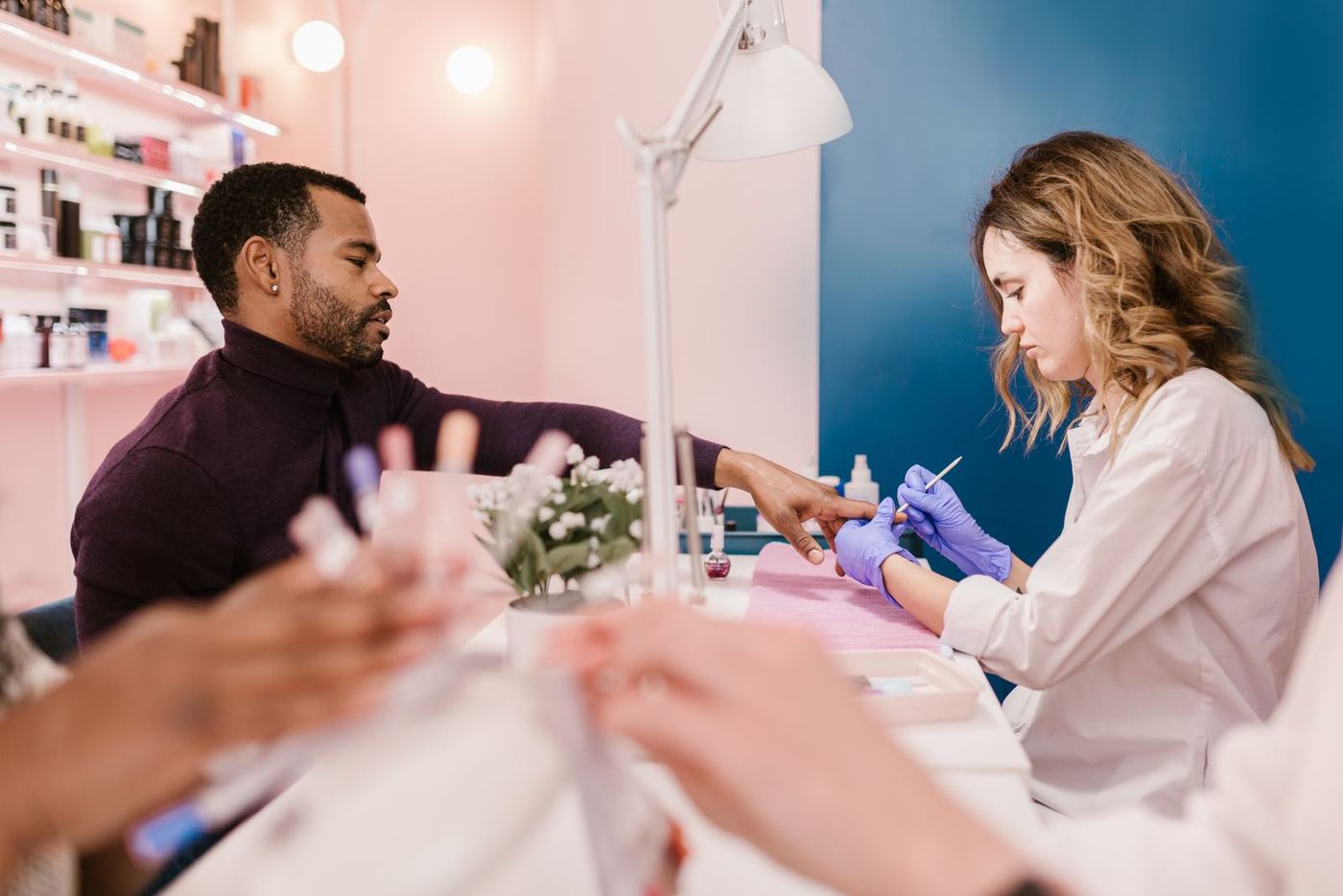 Un salon à plusieurs postes : une prothésiste ongulaire travaille, une autre pose au premier plan.